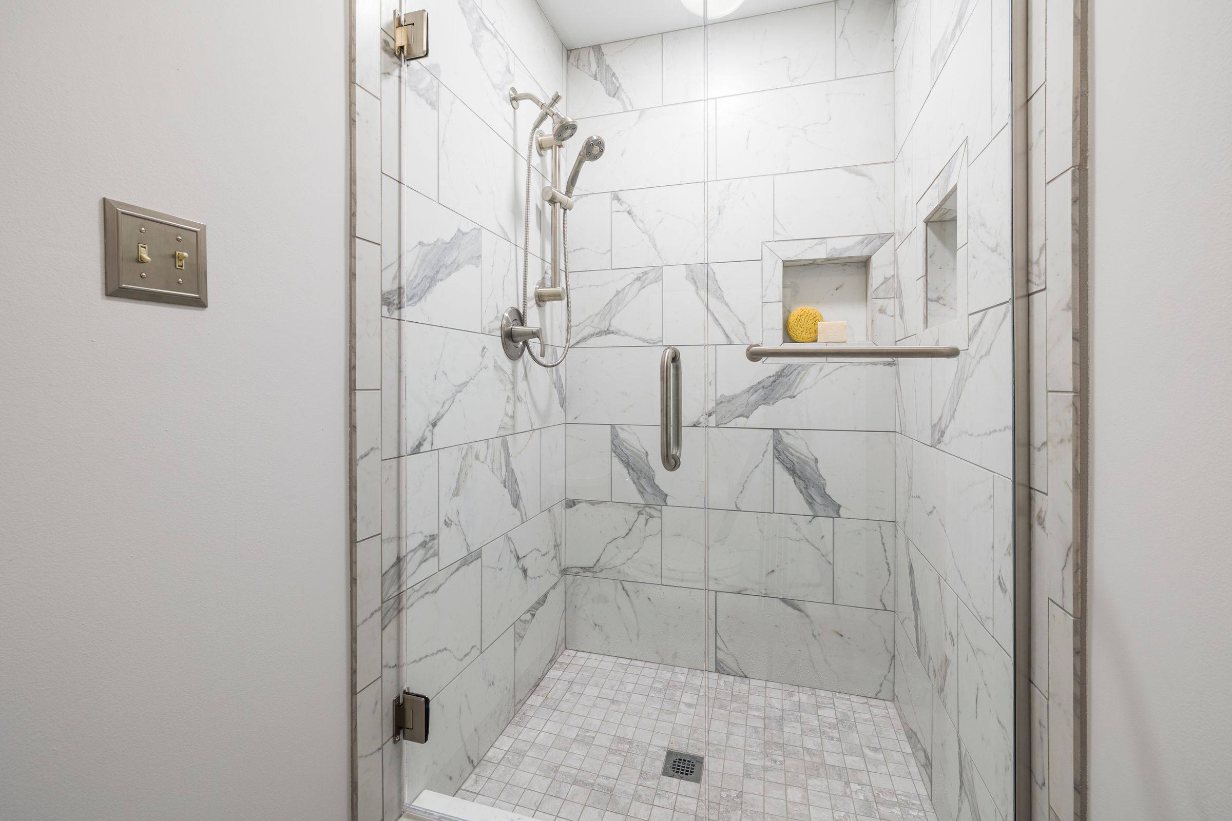 Marble-look tiled shower with a mosaic floor and center drain behind a glass door