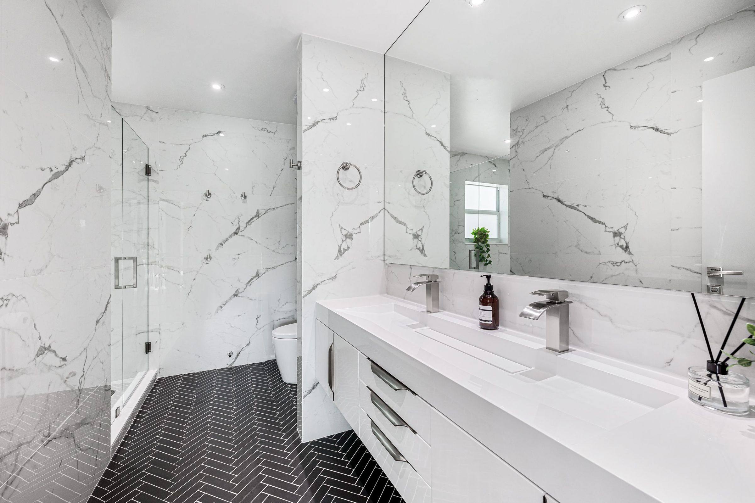 Large-format marble-look wall tile with a black herringbone tile floor